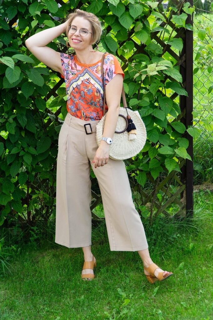 kobieta w pomarańczowej bluzce we wzory i beżowych spodniach